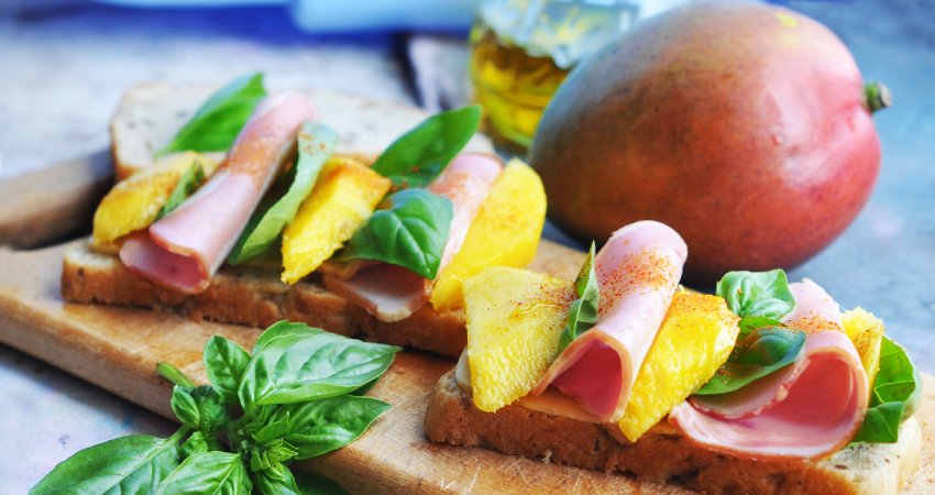 tagliere con bruschette prosciutto crudo e mango, con basilico e un mango intero
